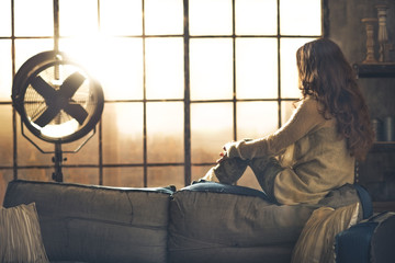 Young woman looking in window in loft apartment. rear view