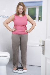 Fototapeta na wymiar Happy Woman Weighing Herself On Scales In Bathroom