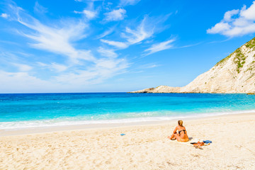 Fototapeta na wymiar Young woman sitting on beautiful Petani beach, Kefalonia island