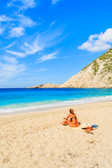 Plakat Young woman sitting on beautiful Petani beach, Kefalonia island