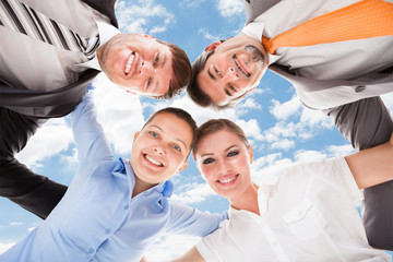 Obraz na płótnie Canvas Happy Business People Forming Huddle Against Sky