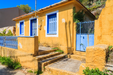 Fototapeta na wymiar Yellow old typical house with blue windows and shutters in Assos