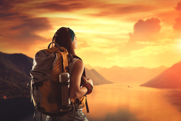 Hiking girl with backpack is looking at sunset