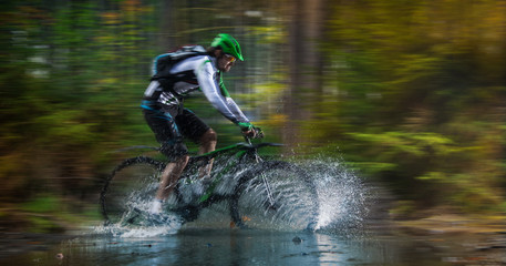 Mountain biker speeding through forest stream.