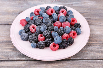 Iced berries on plate, on color wooden background