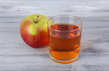 glass of apple juice and fresh apple on grey wooden table
