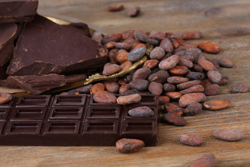 Cracked chocolate bar and cocoa beans on wooden background