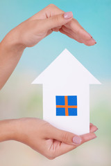 Woman hands holding paper house on bright background