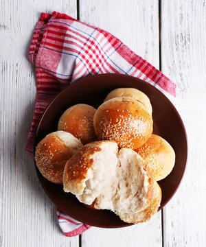 Tasty buns with sesame on plate, on color wooden background