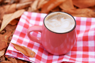 Cup of tasty hot drink on napkin, on autumn leaves background