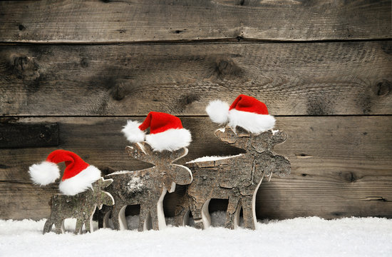 Three mooses wearing santa hats on grey wooden background