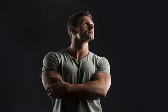 Handsome muscular fit young man on dark background looking up