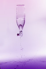 Clear water spill from a glass bottle on purple background on sh