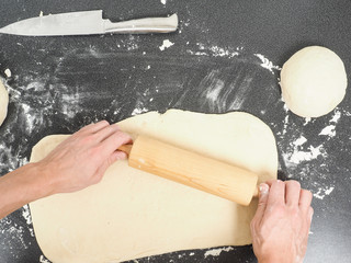 Person handling a dough with a rolling pin floured black table © AB Photography