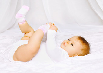 Cute baby in socks lying on the bed and holding legs