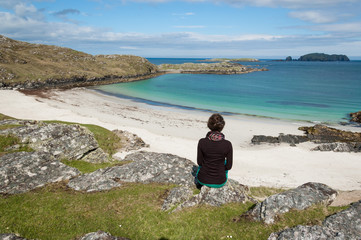 Young woman tourist sitting in front of a desert white beach
