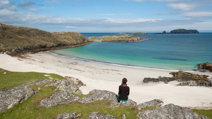 Young woman tourist sitting in front of a desert white beach