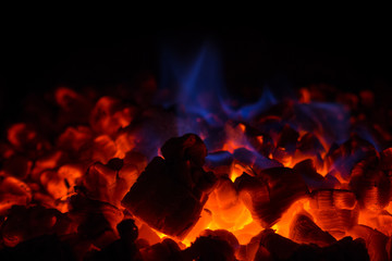 Closeup of glowing hot red embers and blue flame in fireplace
