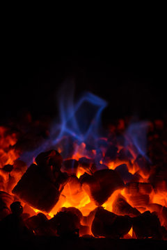 Closeup of glowing hot red embers and blue flame in fireplace