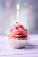 Delicious birthday cupcake on table on light background