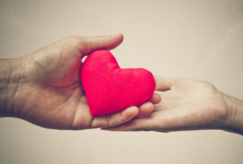 man's hand and woman's hand holding a red heart