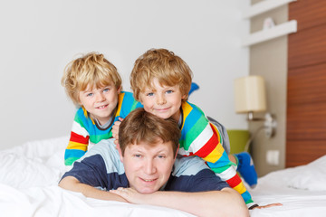 Two little sibling kid boys and dad having fun in bed after slee