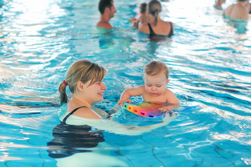 Little baby boy and his mother learning to swim in an indoor swi