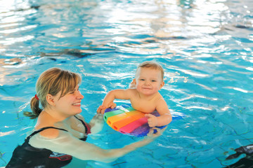 Little baby boy and his mother learning to swim in an indoor swi