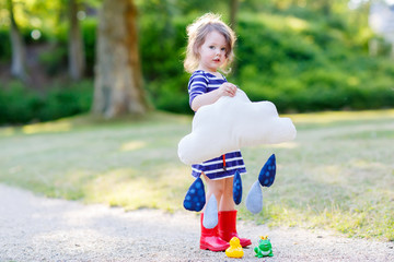 Beautiful little girl in red rain boots playing with toy raindro