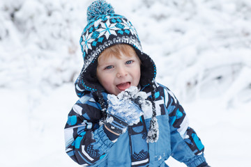 Adorable toddler boy having fun with snow on winter day