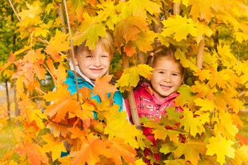 Girl and boy hiding in yellow autumn leaves