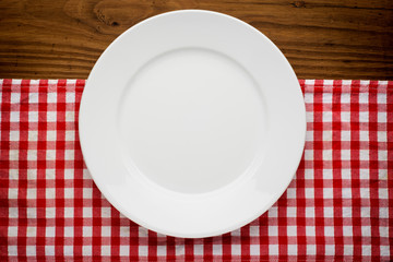 Empty plate with fork and knife on tablecloth over wooden