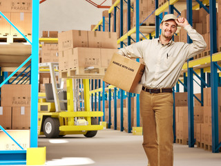 delivery man smiling with a parcel and in uniform inside a warehouse. shipping and logistics...