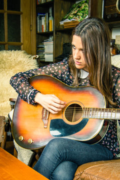 Young hipster girl playing acoustic guitar at home