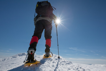 Hiker snowshoeing in winter mountains during sunny day