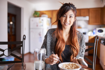 asian teen girl in kitchen eating breakfast with smartphone