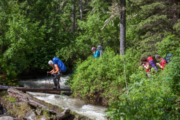 Backpacker is crossing mountain river by wooden log in Altai mou