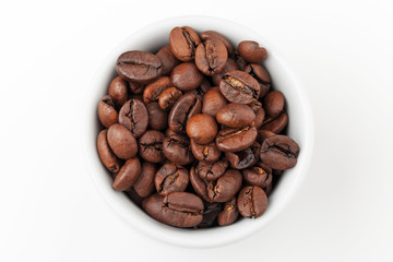 Small white espresso cup full of fresh roasted coffee beans on w