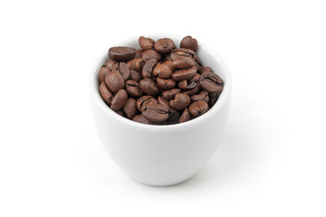 Small white espresso cup full of fresh roasted coffee beans on w