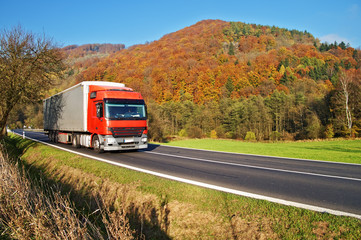 Red truck on the road under the wooded mountain of autumn colors
