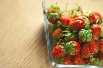 Strawberry fruit in a glass container on a wooden surface. Bokeh