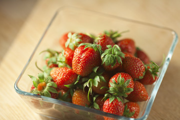 Strawberry fruit in a glass container on a wooden surface. Bokeh