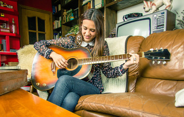 Young hipster girl playing acoustic guitar at home