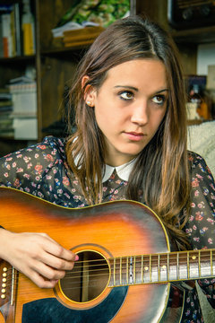 Young hipster girl playing acoustic guitar at home