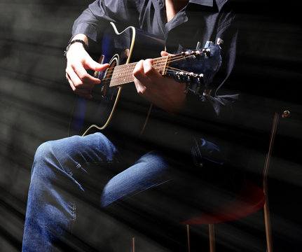 Young musician playing acoustic guitar on dark background