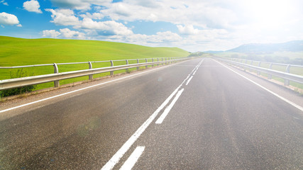 Long way between green fields with blue sky in the background