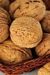 Whole walnuts in a wicker basket on rustic, wooden background