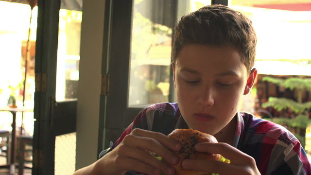 Young teenager eating hamburger in fast food restaurant