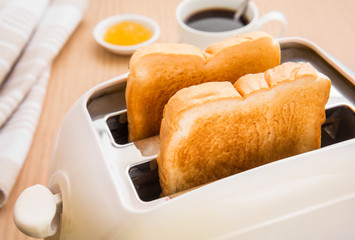 Bread slices in toaster with coffee and jam