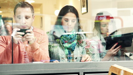 Friends using smartphone, tablet computer and eating in cafe